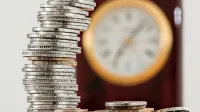 Uhr mit einem Münzstapel davor - BU-Leistungspraxis 2021 – Wie wird Berufsunfähigkeit festgestellt und wie läuft die Leistungsprüfung?