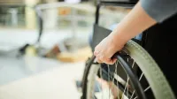 Hand eines Rollstuhlfahrers am Reifen des Rollstuhls- Trends zur Grundfähigkeitsversicherung