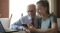 Eine junge Frau sitzt mit ihrem Großvater am Tisch und sie schauen zusammen in ein Laptop - Vergleich von Rentenfaktoren