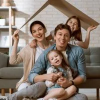 Franke und Bornberg Rating Komposit Wohngebäude - Familie sitzt im Wohnzimmer unter einem spielerischen Papphaus-Dach